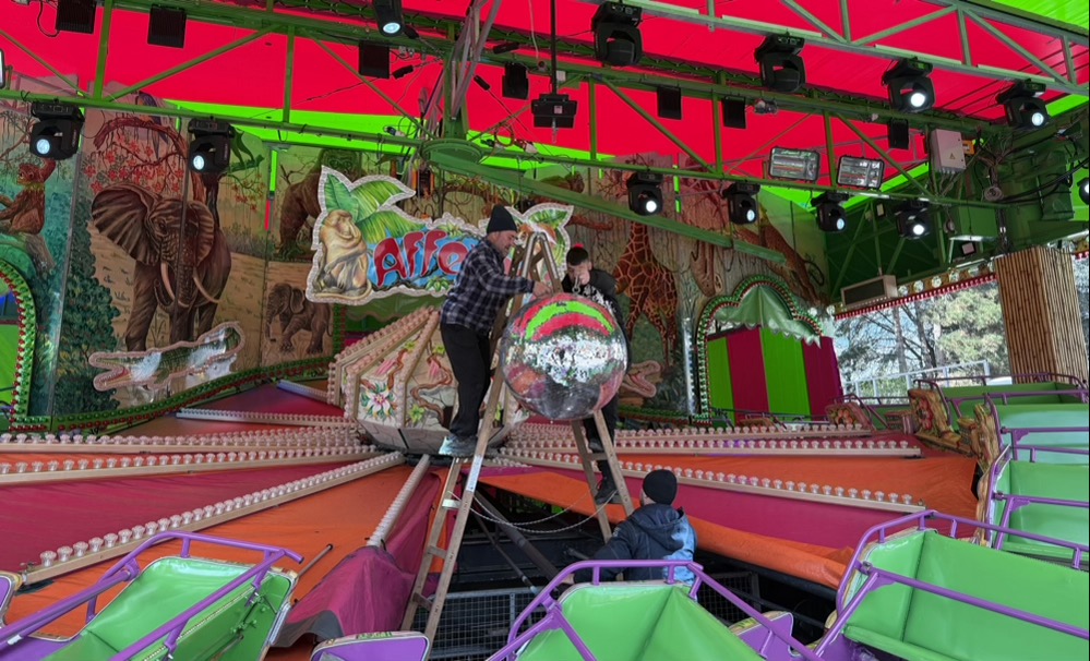 Arbeiter hängen eine Discokugel in einem Fahrgeschäft auf.