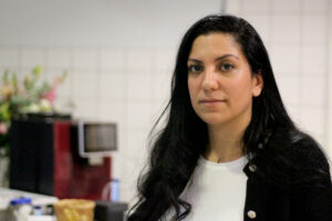 Selvi Aksünger steht vor der Cafeteriatheke und schaut in die Kamera. Immer Hintergrund ist eine rote Kaffeemaschine zu sehen.