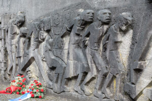 In Stein gemeißelte Figuren. Auf dem Boden zwei Blumenkränze.