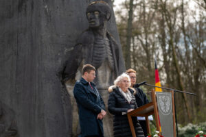 Im Hintergrund das Mahnmal Bittermark. Im Vordergrund drei Menschen an dem Rednerpult.