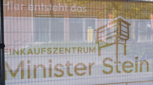 Ein Baugitter auf dem das Logo aufgespannt wurde. Darüber steht "Hier entsteht das". Der Druck ist in weiß und okker gestaltet.