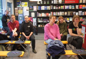 Frauen und Männer sitzen auf Holzbänken