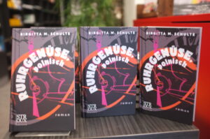 Drei Bücher stehen mit dem Titel zu den Betrachter*innen. 