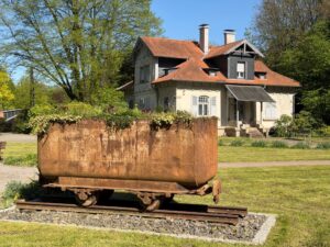 Friedhof und Bergbau treffen aufeinander: Die Lore auf dem Eingangsrondell mit historischem Gebäude im Hintergrund.