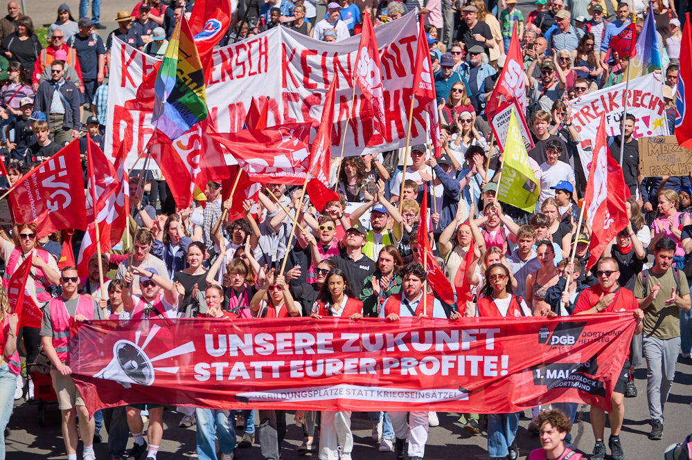 Menschenmenge bei einer Demonstration in Dortmund mit roten Fahnen und einem großen roten Banner mit der Aufschrift 'UNSERE ZUKUNFT STATT EURER PROFITE!'