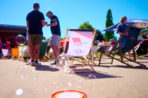 Mehrere Menschen sitzen und stehen im Westfalenpark Dortmund auf Liegestühlen bei sonnigem Wetter, im Vordergrund sind schwebende Seifenblasen zu sehen.