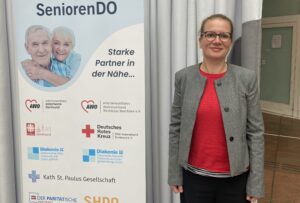 Prof. Martina Brandt neben dem Banner „SeniorenDO“. 