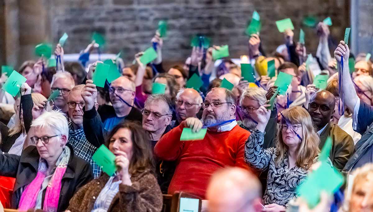 Blick in den Saal - das Bild zeigt Menschen bei der Abstimmung mit Stimmkarten