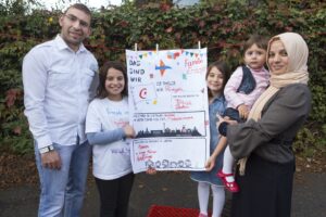 Mutter, Vater und drei Kinder, die ein Plakat präsentieren.