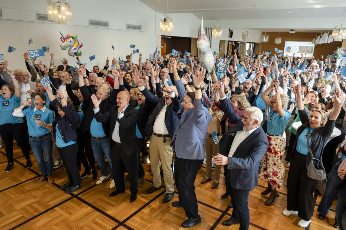 Jubelnde Menschen in einem Saal.