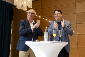 Zwei Männer stehen an einem Tisch und klatschen.