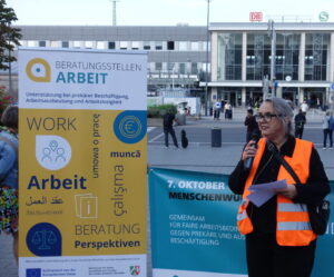 Eine Frau in Warnweste steht vor Plakaten und hält eine Rede