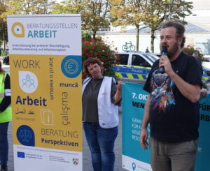 Ein Mann mit Mikrofon spricht zu Demonstrant:innen.
