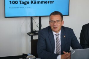 Mann im Anzug sitzt vor einem Beamer mit der Aufschrift : 100 Tage Kämmerer