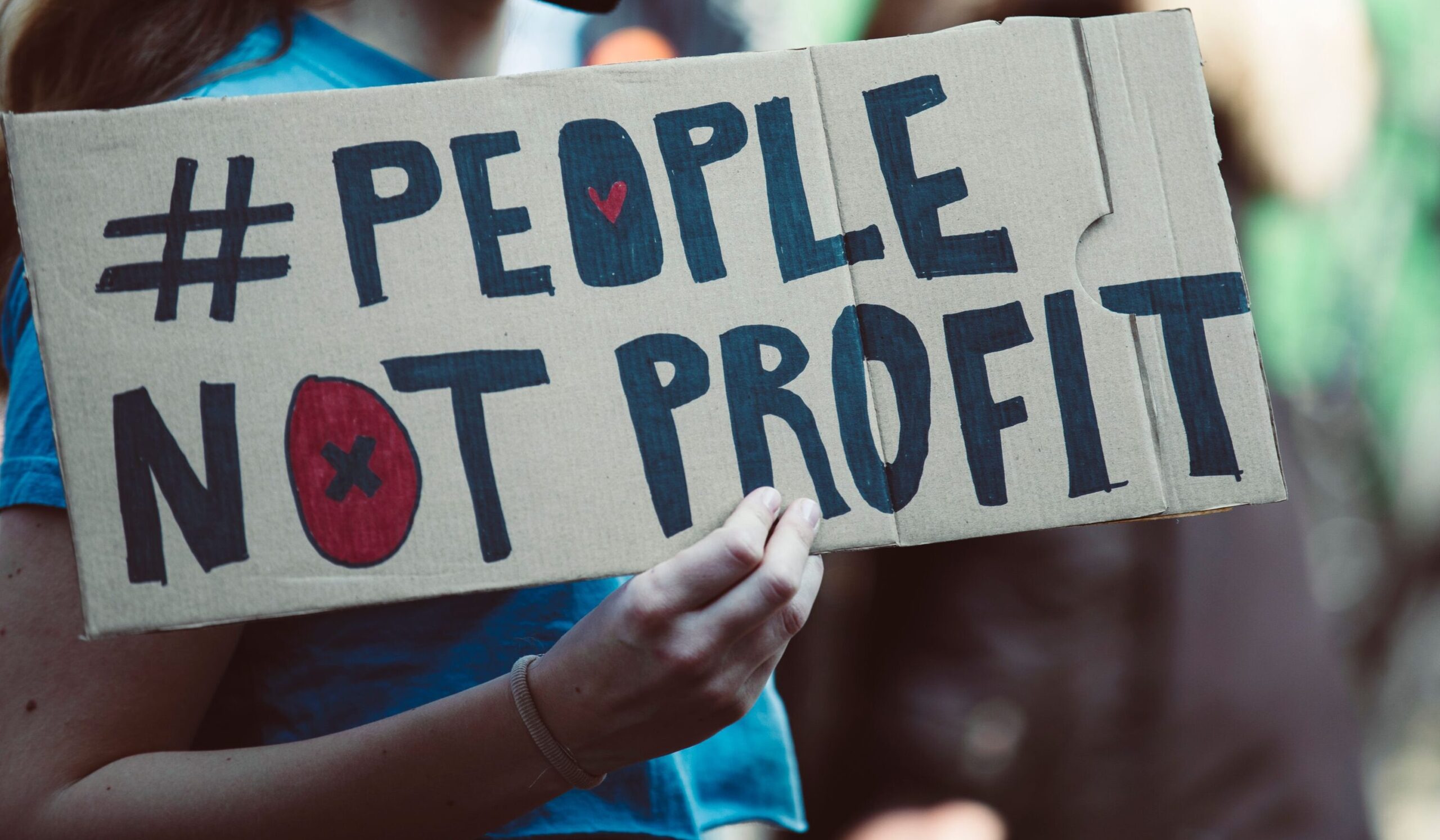 Auf dem Bild ist eine Hand, die ein Plata hochhält. Dort steht drauf: "People not Profit".