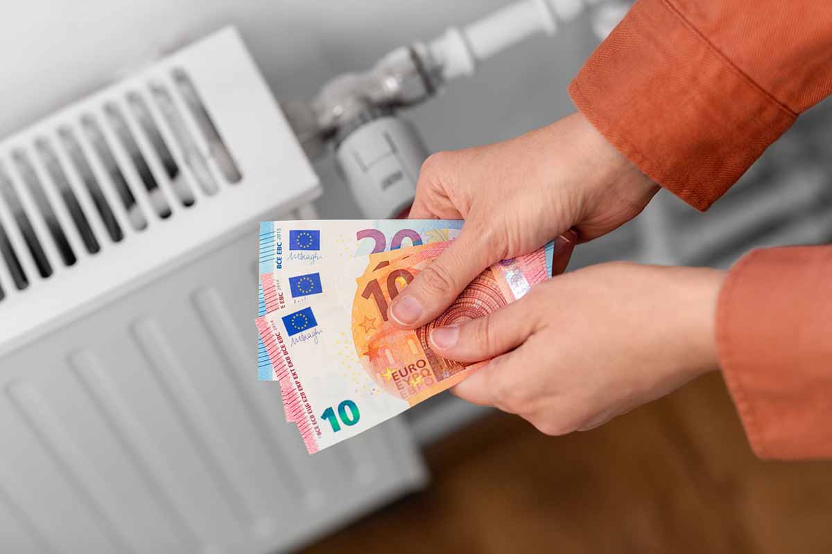 Eine Person hält Geldscheine über einen Heizkörper
